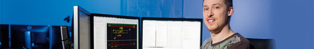 Junger Mitarbeiter auf Bürostuhl vor 3 Displays